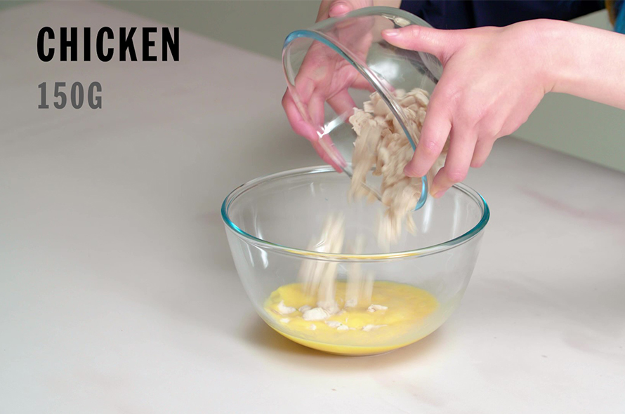 Pouring a bowl of shreaded chicken into a bowl of whisked eggs